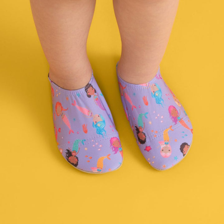 Lifestyle image of little one wearing mermaid beach shoes over yellow floor.