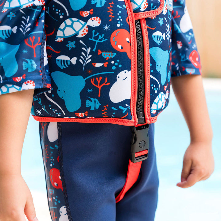 Lifestyle image of child wearing neoprene swim vest with non-removable floats in navy, red trims, and sea life themed print. Front.