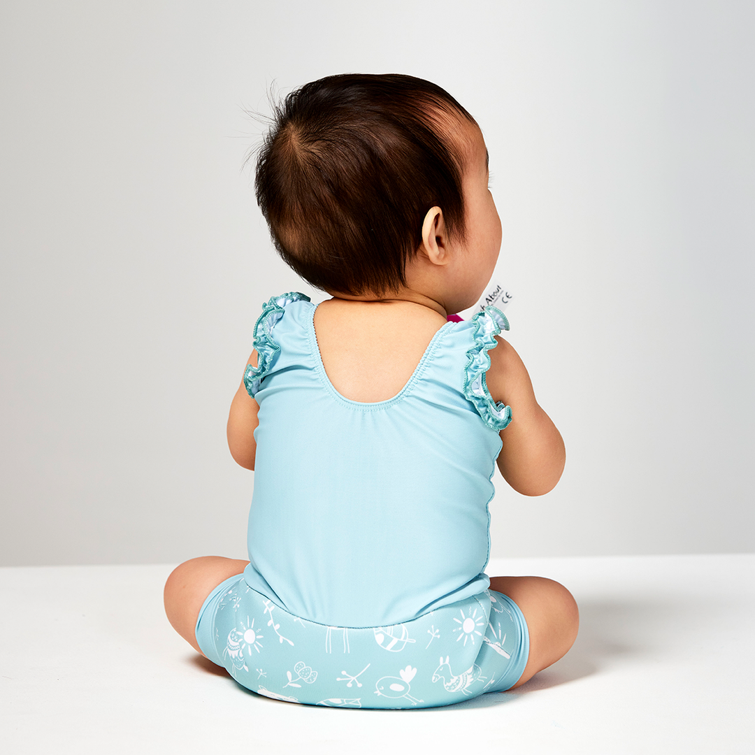 Lifestyle image of child wearing a Happy Nappy Costume in greenish blue featuring animals themed print, including bears, birds and llamas. Back.