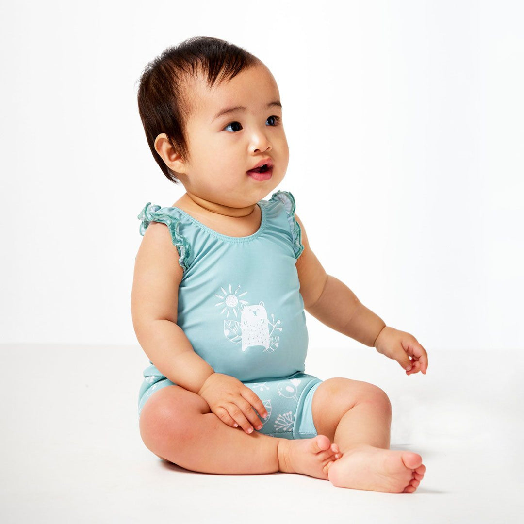 Lifestyle image of child wearing a Happy Nappy Costume in greenish blue featuring animals themed print, including bears, birds and llamas. Front.