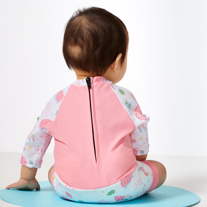 Lifestyle image of child wearing Happy Nappy Sunsuit in pink and forest themed print, including hedgehogs, mushrooms and leaves. Back.