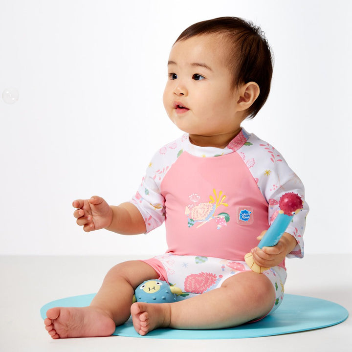 Lifestyle image of child wearing Happy Nappy Sunsuit in pink and forest themed print, including hedgehogs, mushrooms and leaves. Side.