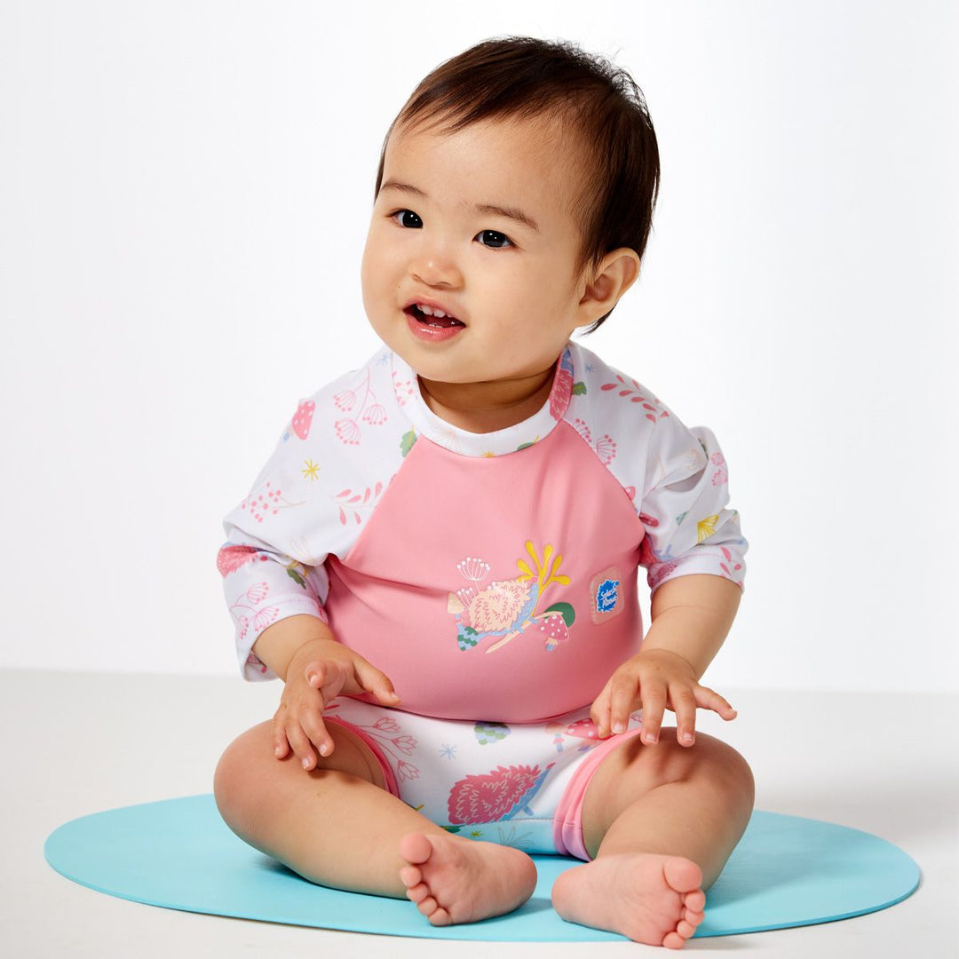 Lifestyle image of child wearing Happy Nappy Sunsuit in pink and forest themed print, including hedgehogs, mushrooms and leaves. Front.