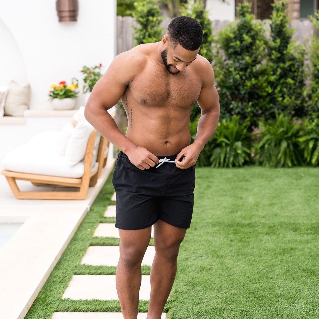 Man wearing black swim shorts for men in black by the pool.