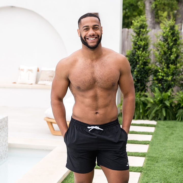Man wearing black swim shorts for men in black by the pool.