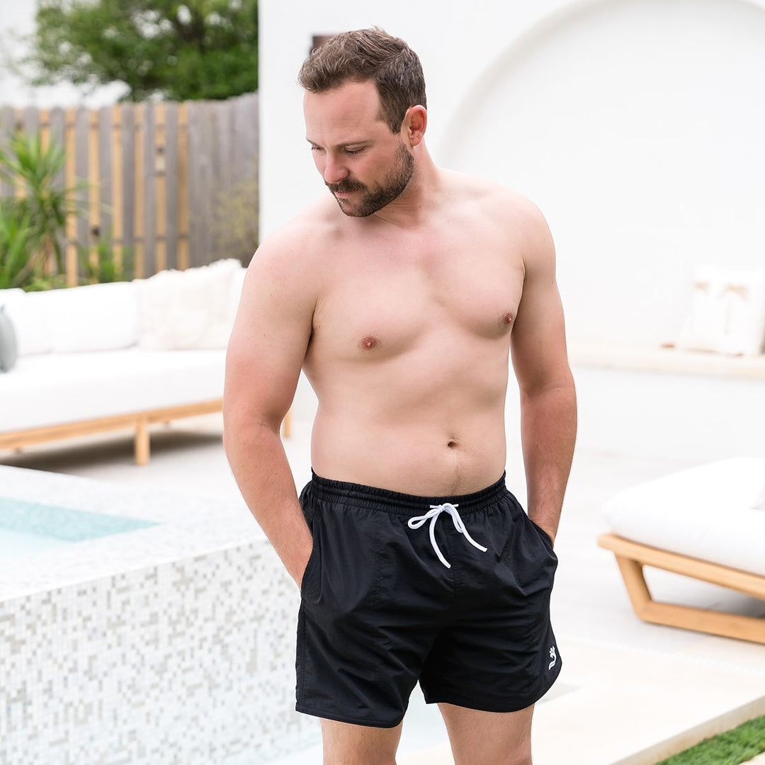 Man wearing black swim shorts for men in black by the pool.