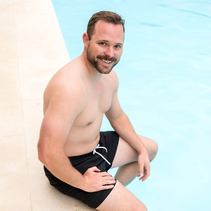 Man wearing black swim shorts for men in black by the pool.