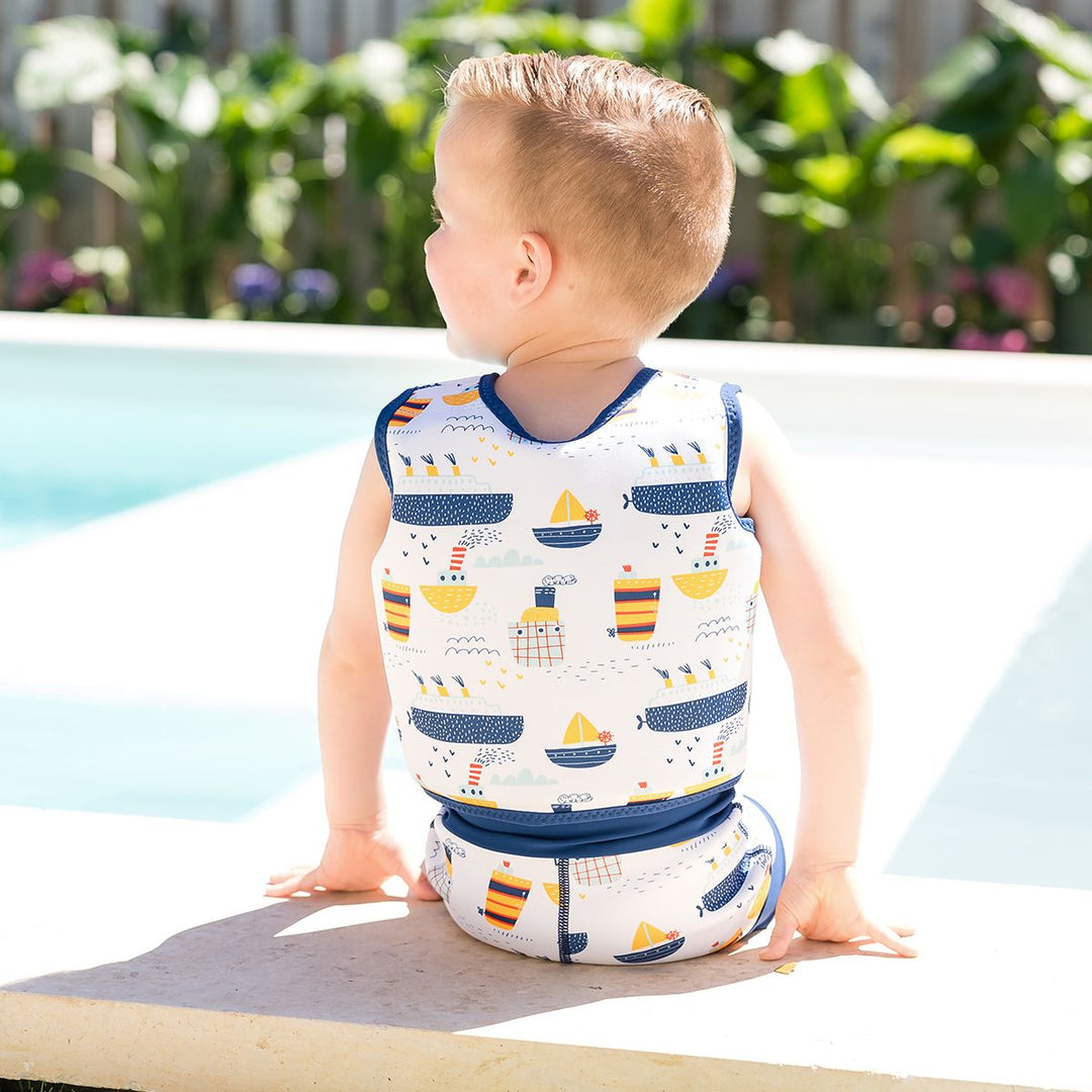 Lifestyle image of child wearing neoprene swim vest for toddlers with non-removable floats in white, navy trims and boats themed print. He's also wearing matching Happy Nappy. Back.