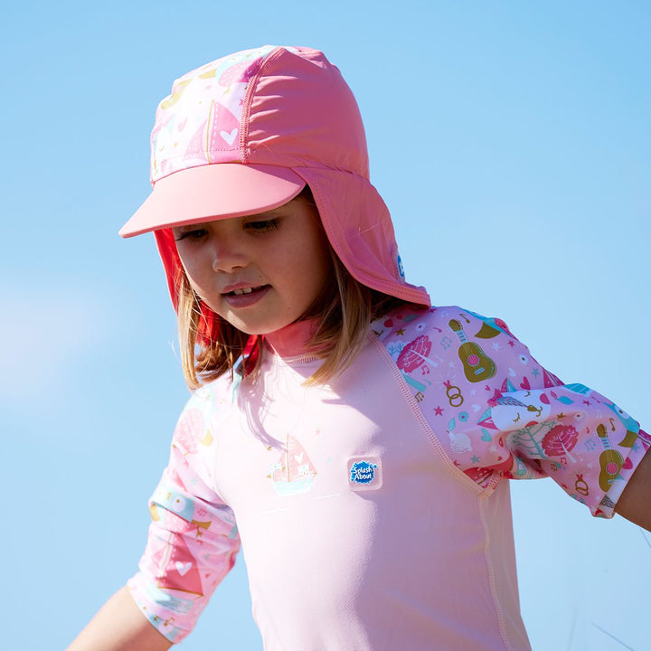 Lifestyle image of toddler wearing a legionnaire style sun hat in the beach. The hat is reddish pink and baby pink, with the owl and the pussycat themed print panel. She's also wearing matching sun and sea wetsuit. Close-up.
