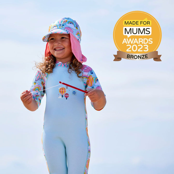 Lifestyle image of a child wearing a one piece UV sun and sea wetsuit for toddlers in light blue. Hot air balloons themed print including clouds and rainbows on sleeves, side panels, neck and chest.