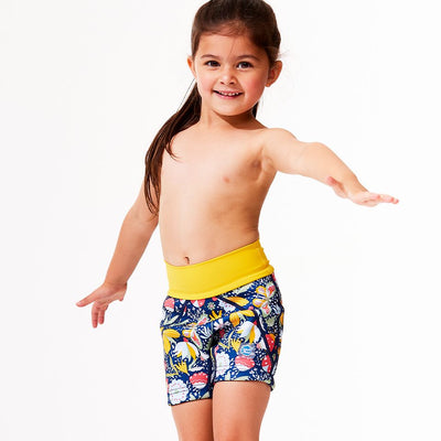 Lifestyle image of toddler standing up, wearing neoprene swim shorts in navy blue with yellow waist and floral print.