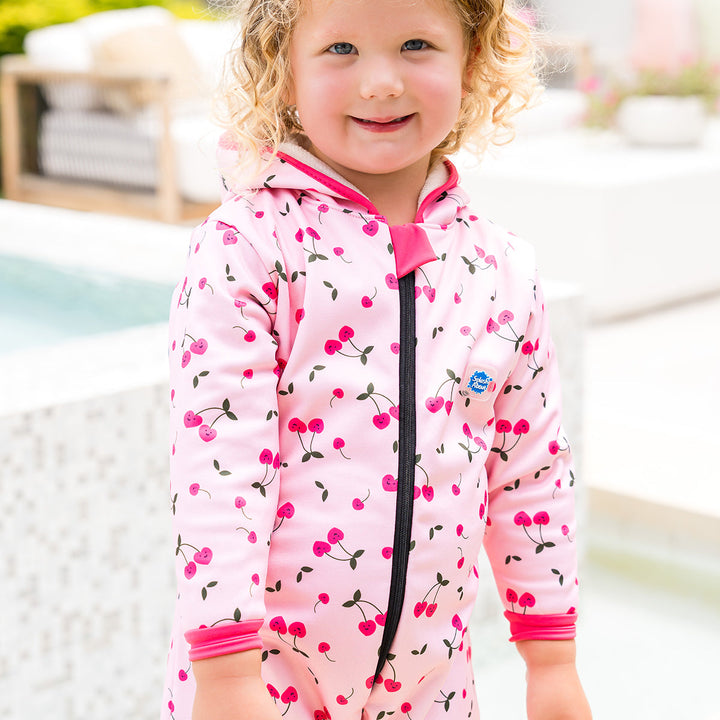 Little one wearing waterproof fleece-lined onesie with hood in pink and cherries themed print. Hot pink trims.