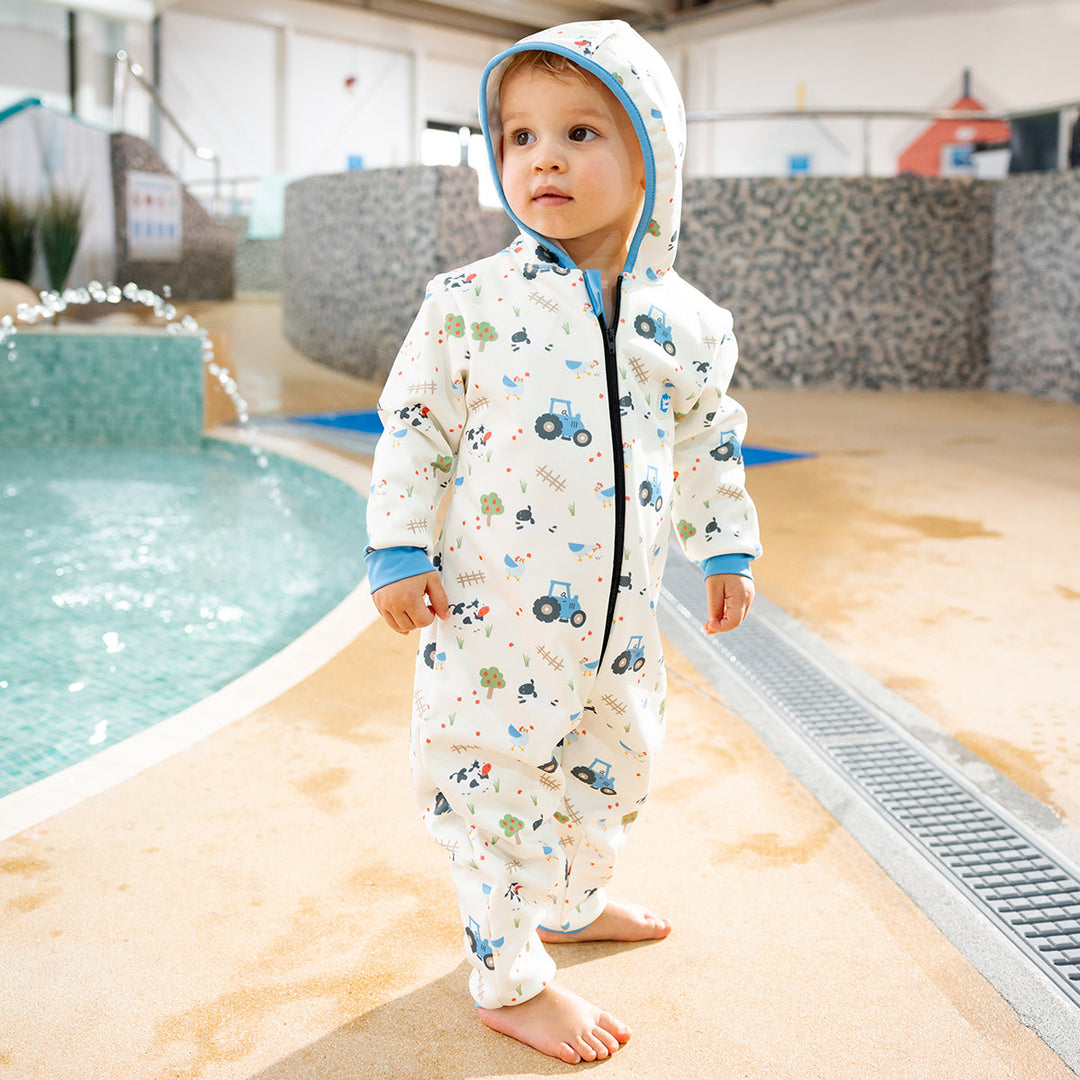 Little one wearing waterproof fleece-lined onesie with hood in white and farm themed print. Blue trims.