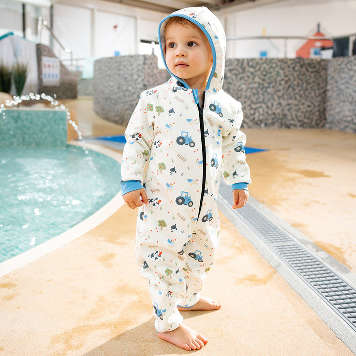 Little one wearing waterproof fleece-lined onesie with hood in white and farm themed print. Blue trims.
