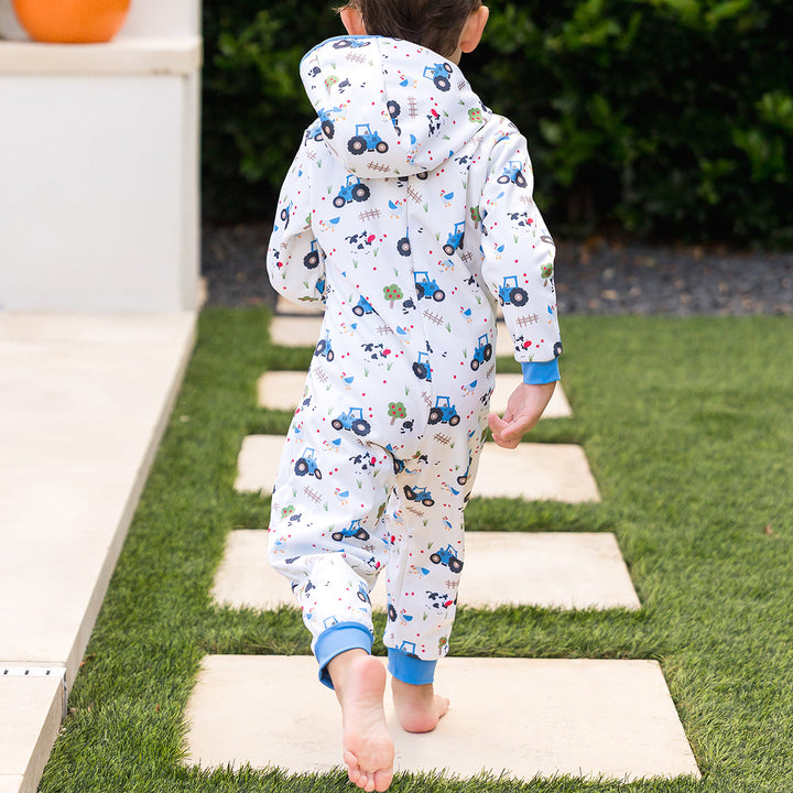 Little one wearing waterproof fleece-lined onesie with hood in white and farm themed print. Blue trims.