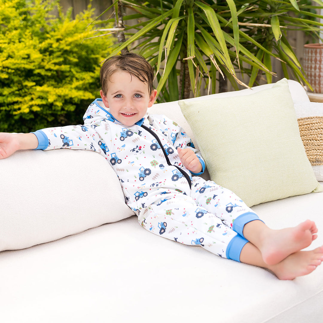 Little one wearing waterproof fleece-lined onesie with hood in white and farm themed print. Blue trims.