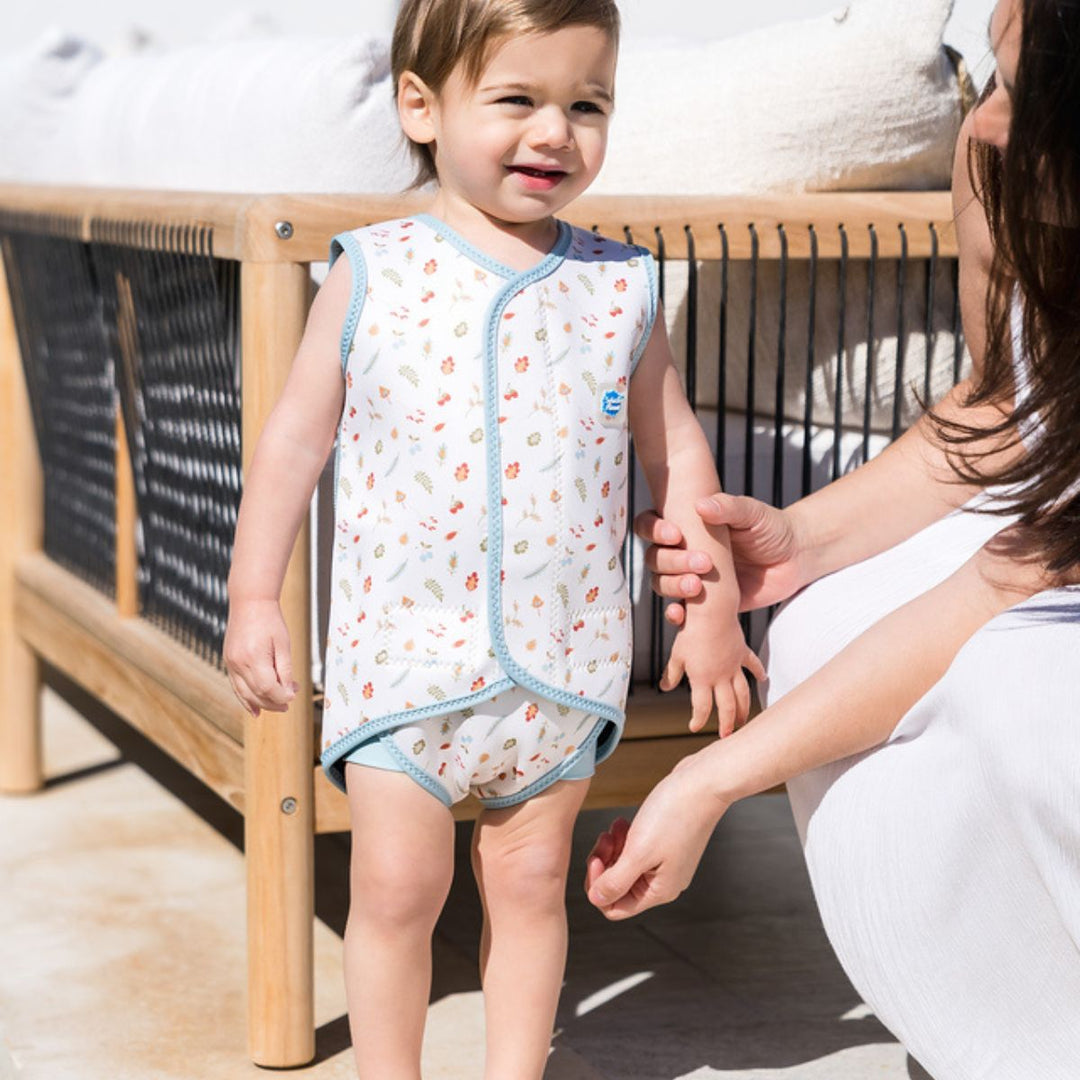 Child wearing neoprene baby wrap wetsuit in white with blue trims and autumn themed print.