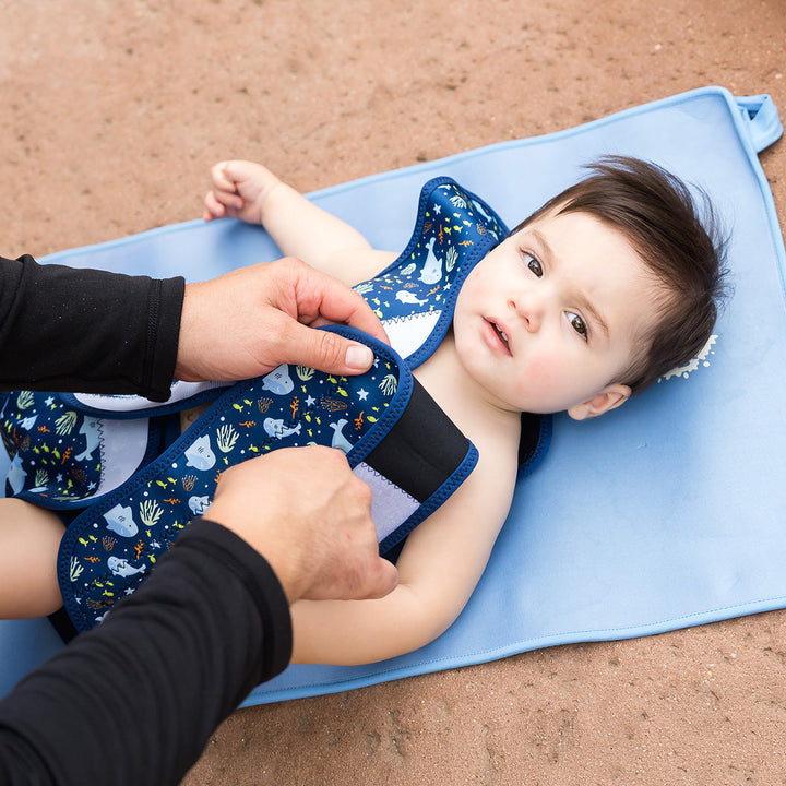Little one wearing neoprene baby wrap wetsuit in navy and sharks themed print.