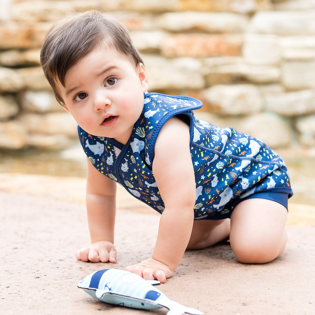Little one wearing neoprene baby wrap wetsuit in navy and sharks themed print.