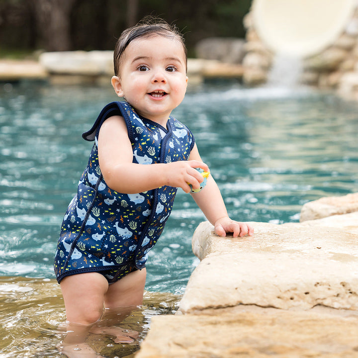 Little one wearing neoprene baby wrap wetsuit in navy and sharks themed print.