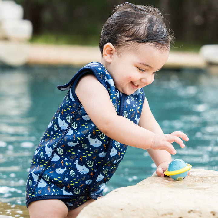 Little one wearing neoprene baby wrap wetsuit in navy and sharks themed print.