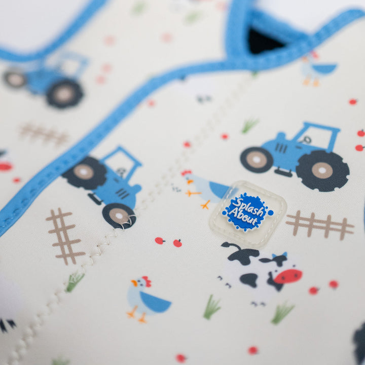 Close up of neoprene baby wrap wetsuit in white with blue trims and farm themed print. 