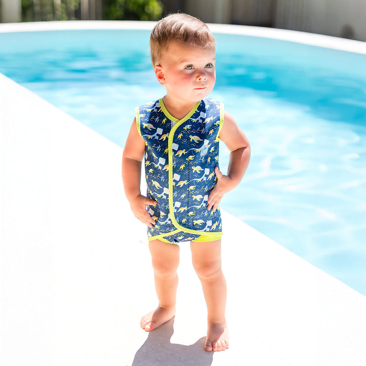 Little one wearing neoprene baby wrap wetsuit in navy with lime trims and turtles themed print.