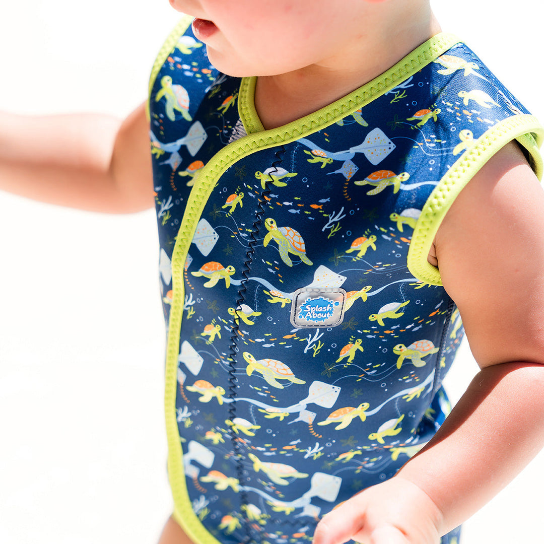 Little one wearing neoprene baby wrap wetsuit in navy with lime trims and turtles themed print.