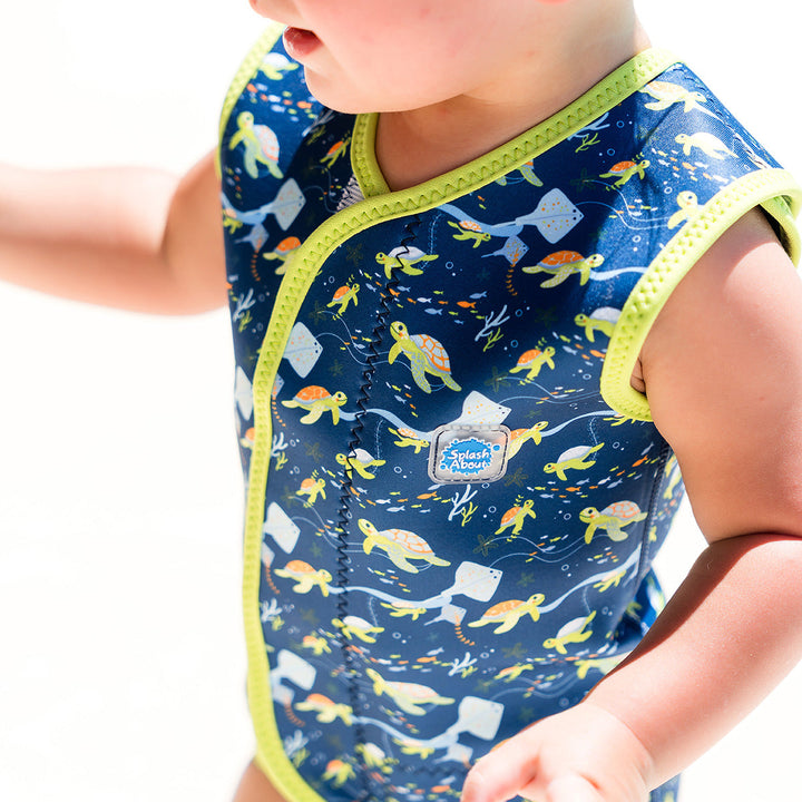 Little one wearing neoprene baby wrap wetsuit in navy with lime trims and turtles themed print.
