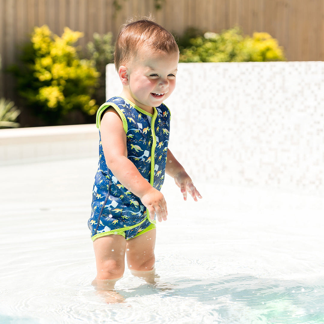 Little one wearing neoprene baby wrap wetsuit in navy with lime trims and turtles themed print.
