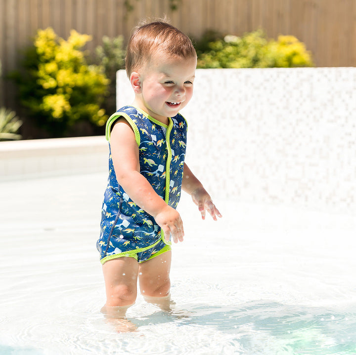 Little one wearing neoprene baby wrap wetsuit in navy with lime trims and turtles themed print.