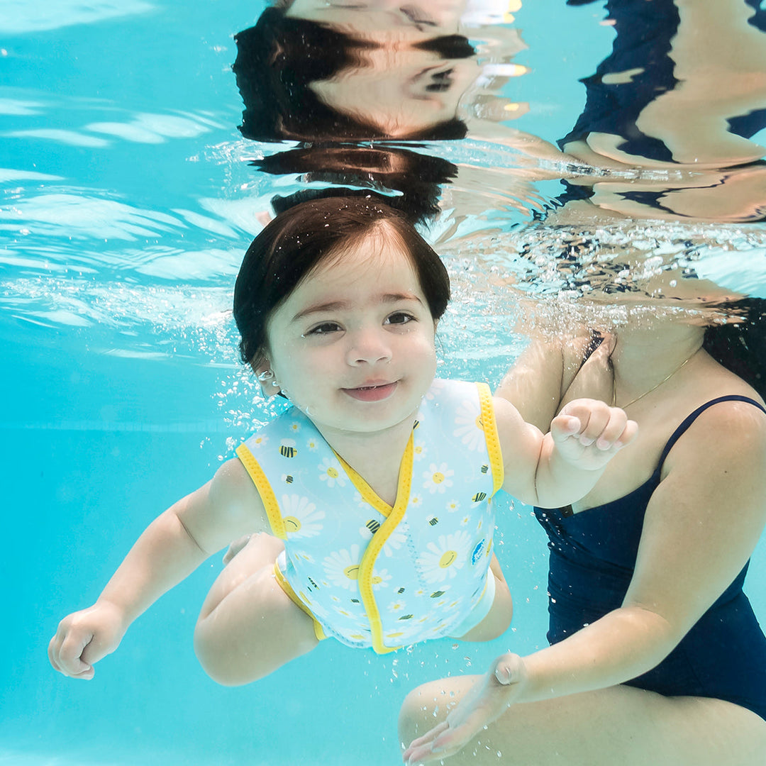Little one wearing neoprene baby wrap wetsuit in baby blue with yellow trims and daisies and bees themed print.