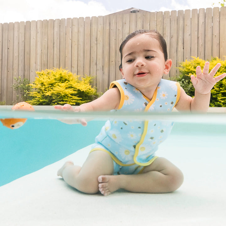 Little one wearing neoprene baby wrap wetsuit in baby blue with yellow trims and daisies and bees themed print.