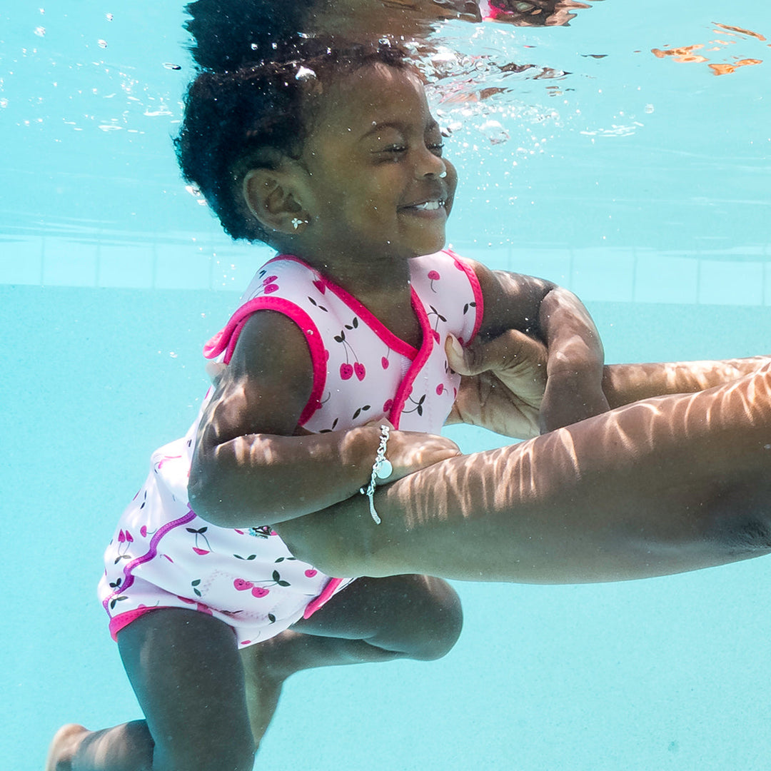 Little one wearing neoprene baby wrap wetsuit in pink and cherries themed print.