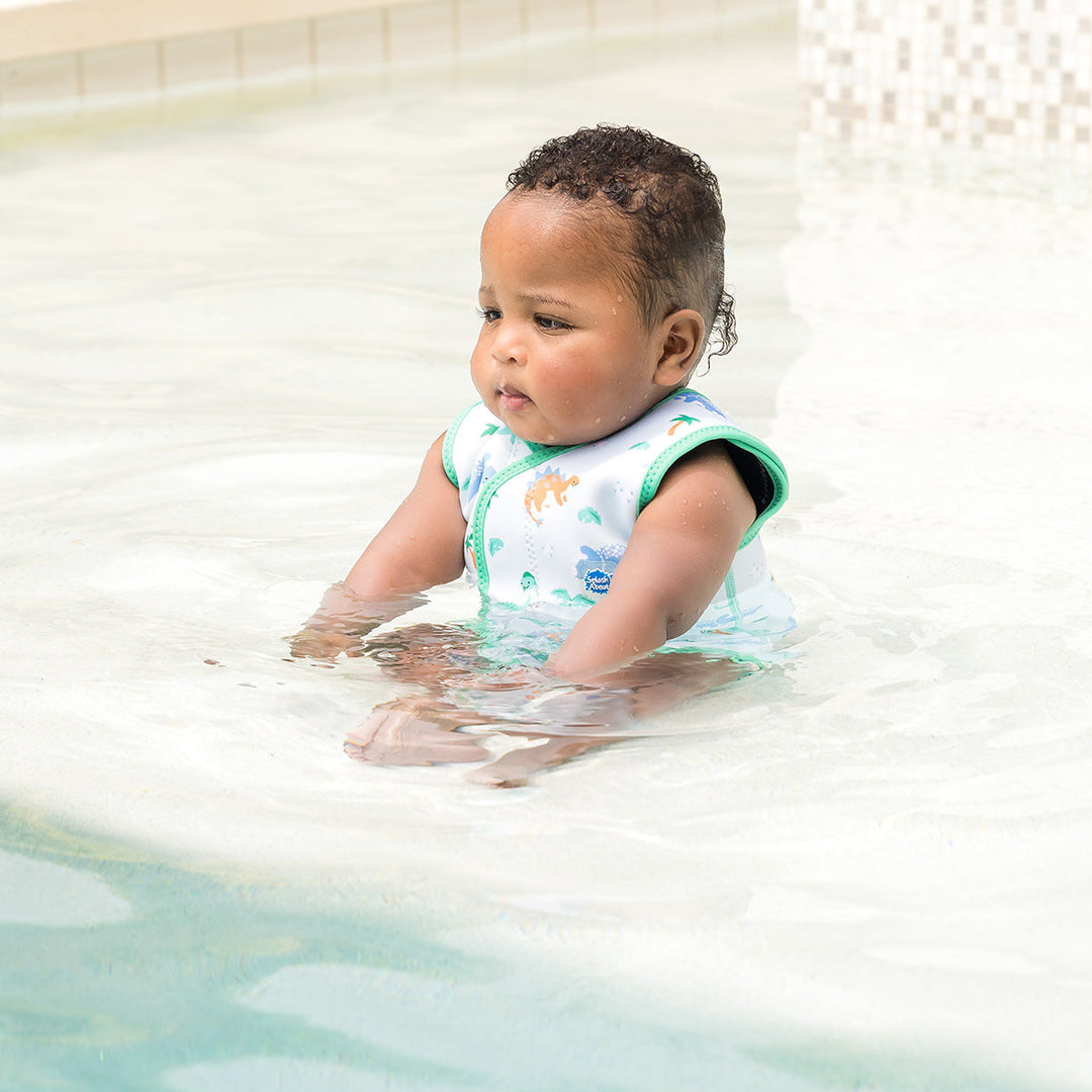 Little one wearing neoprene baby wrap wetsuit in mint and dinosaurs themed print.