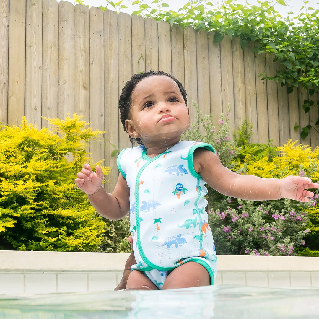 Little one wearing neoprene baby wrap wetsuit in mint and dinosaurs themed print.