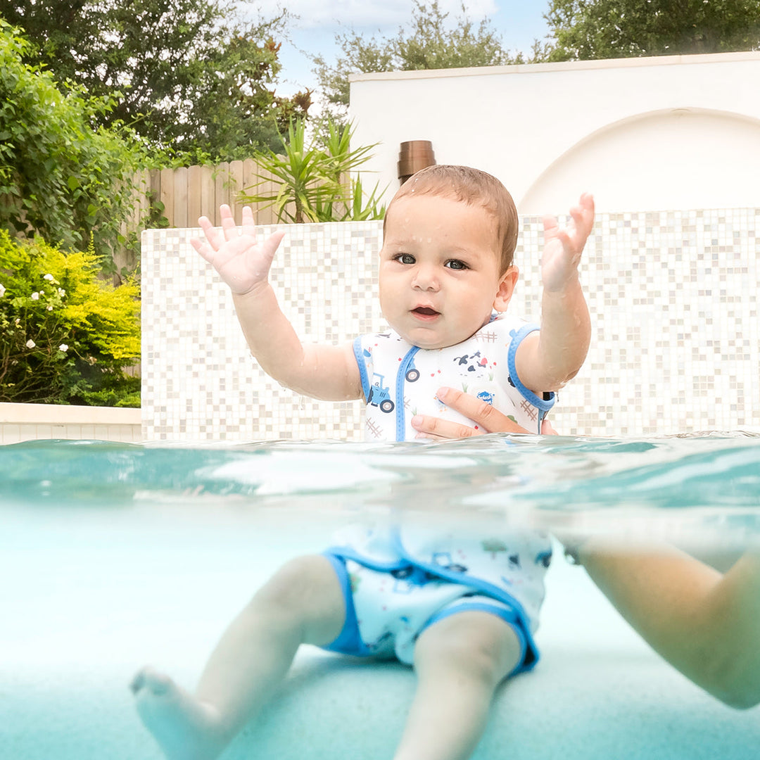 Little one wearing neoprene baby wrap wetsuit in white with blue trims and farm themed print.
