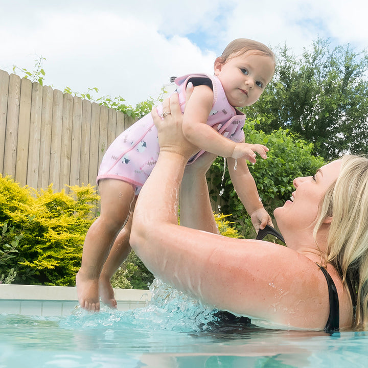 Little one wearing neoprene baby wrap wetsuit in baby pink and sheep themed print.