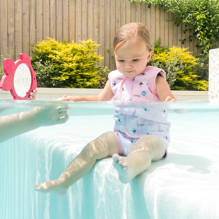 Little one wearing neoprene baby wrap wetsuit in baby pink and sheep themed print.