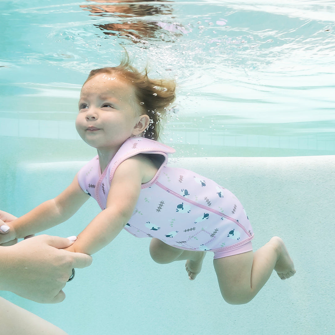 Little one wearing neoprene baby wrap wetsuit in baby pink and sheep themed print.