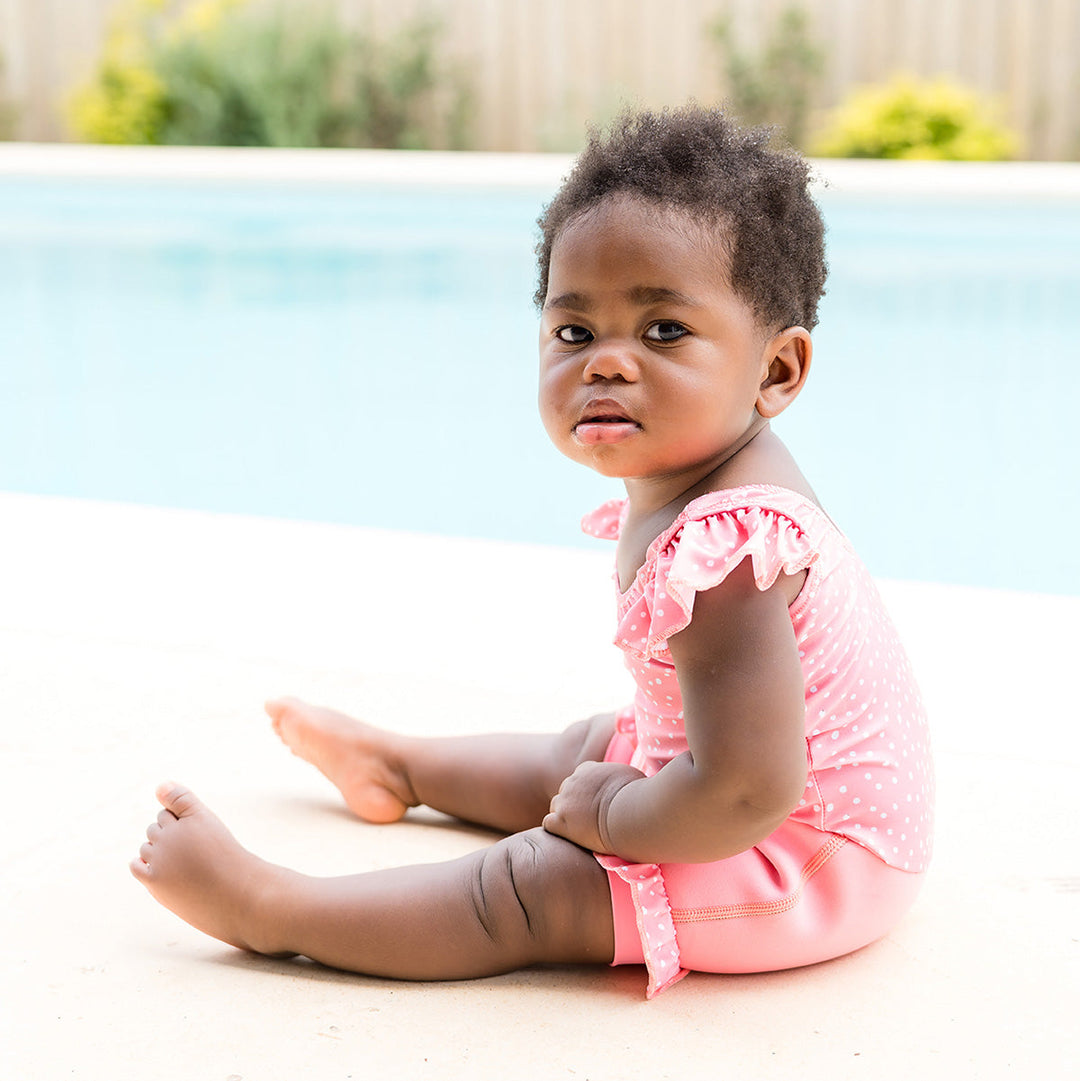 Little one wearing Happy Nappy Costume in pink and white dots, featuring frills in arms and legs.