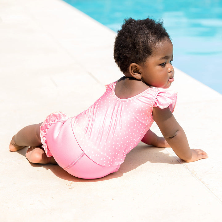 Little one wearing Happy Nappy Costume in pink and white dots, featuring frills in arms and legs.
