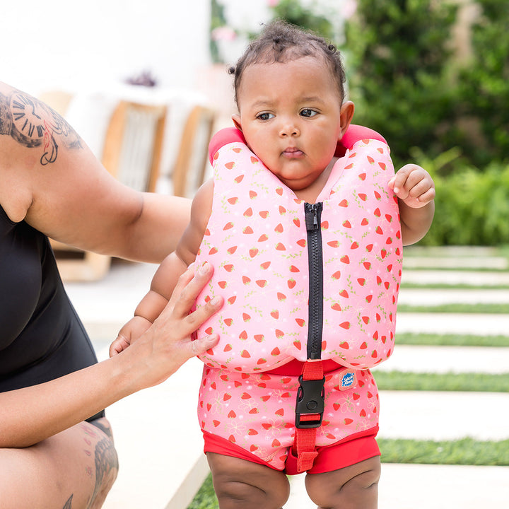 Little one wearing early years swim vest with strawberries print, front zip and bright red trim for kids learn to swim.
