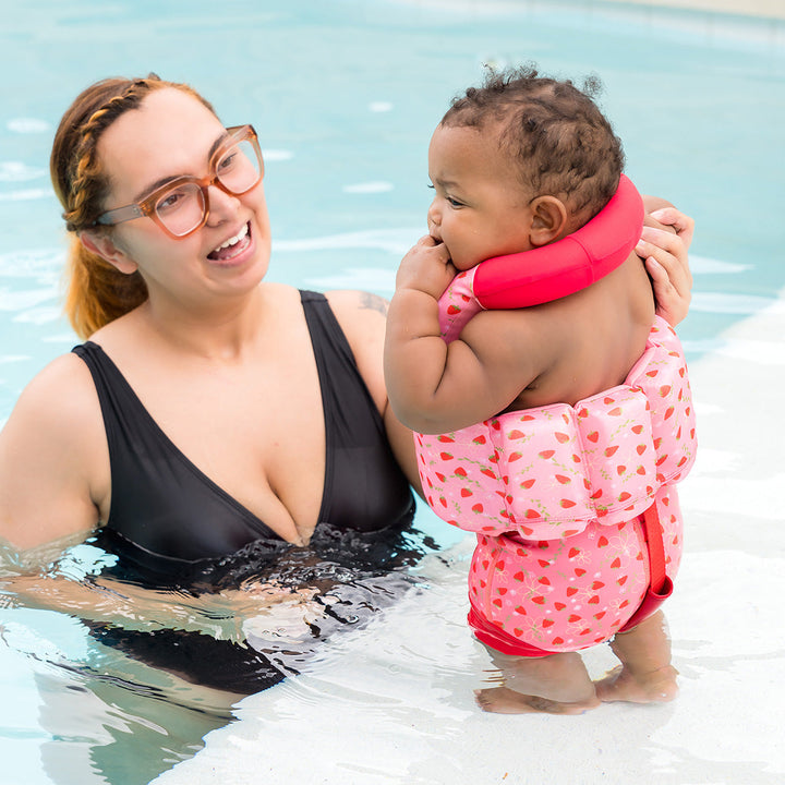 Little one wearing early years swim vest with strawberries print, front zip and bright red trim for kids learn to swim.