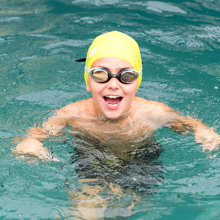 Kid swimming, wearing yellow silicone swim cap.
