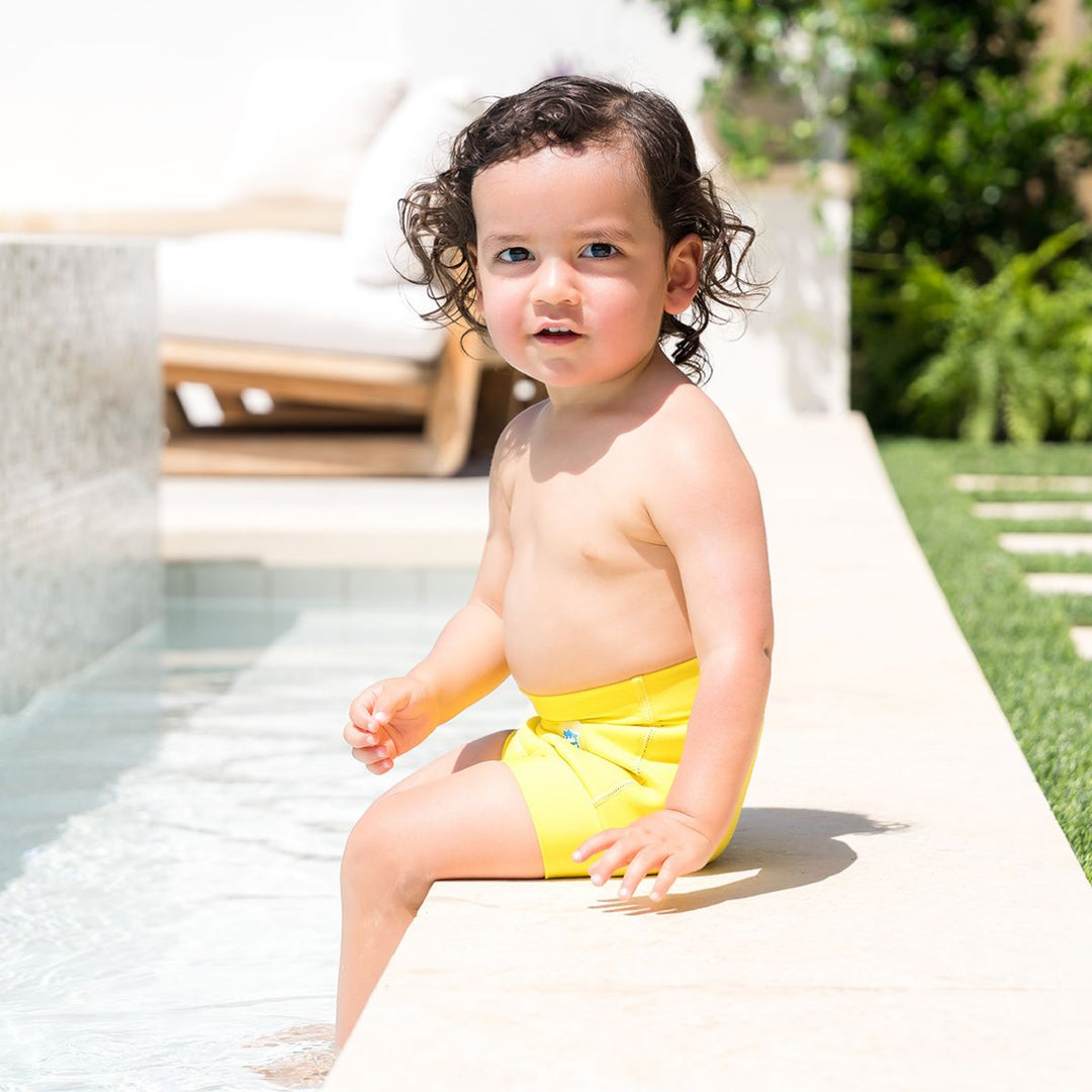 Little one wearing neoprene swim nappy in bright yellow, poolside.