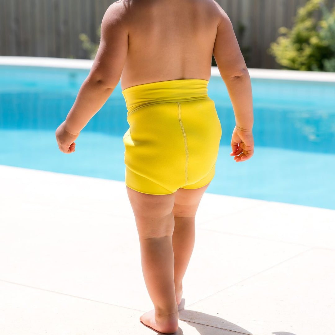 Close up of little one wearing neoprene swim nappy in bright yellow, front.