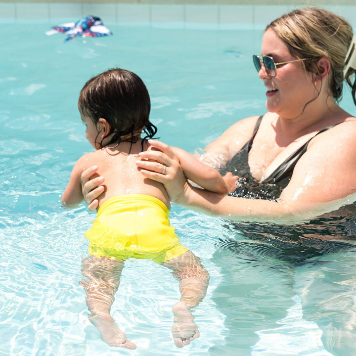 Little one swimming with mum in the pool, wearing neon yellow swim nappy.