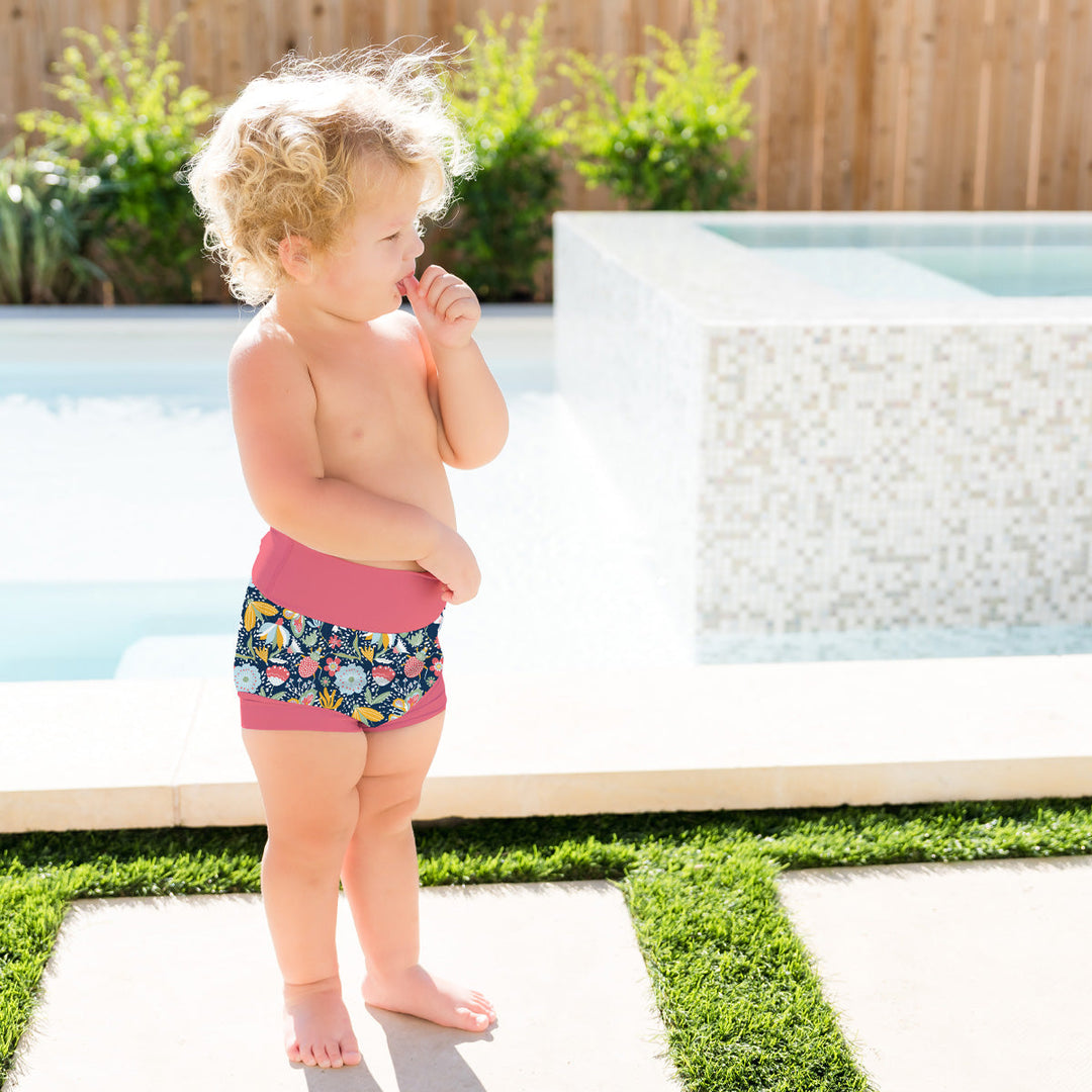 Little one wearing neoprene swim nappy in navy with pink trims, and floral themed print.