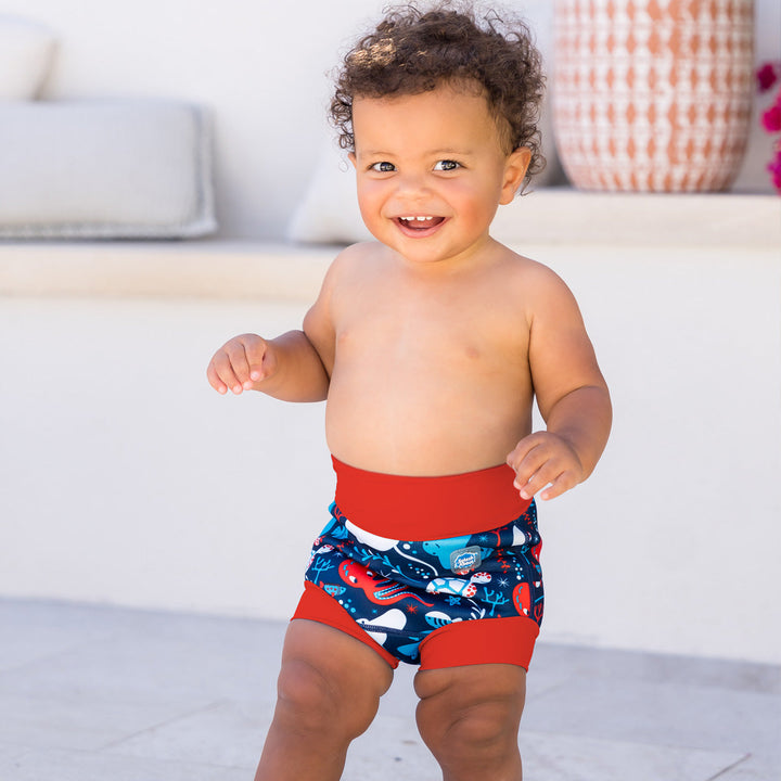 Little one wearing neoprene swim nappy in blue with red ribs, featuring under the sea themed print.
